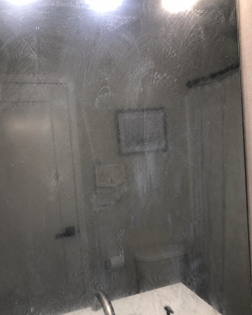 Close-up of a streaky, smeared bathroom mirror with dried-on residue catching the light