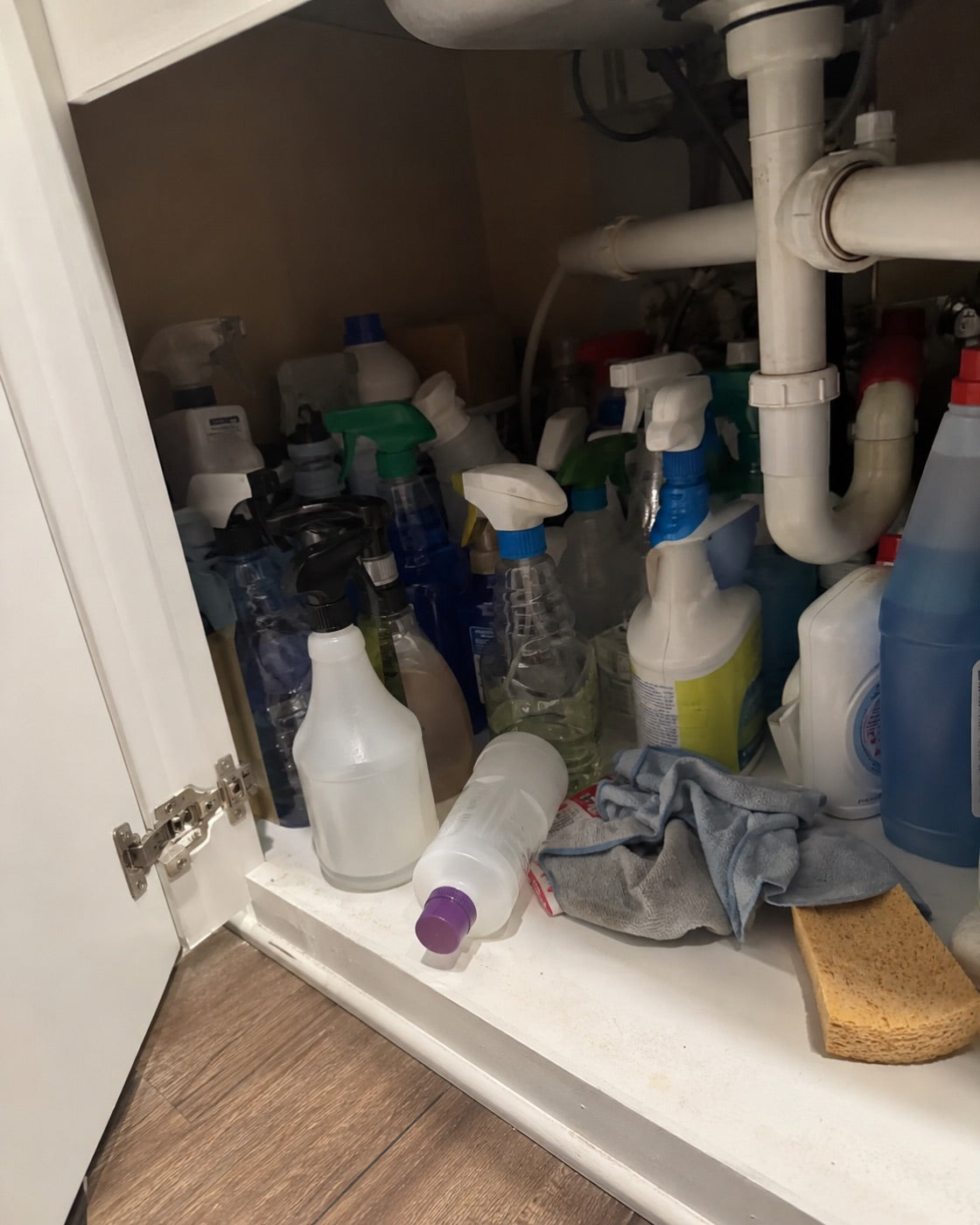 An under-sink cabinet crowded with mismatched single-purpose cleaning bottles.