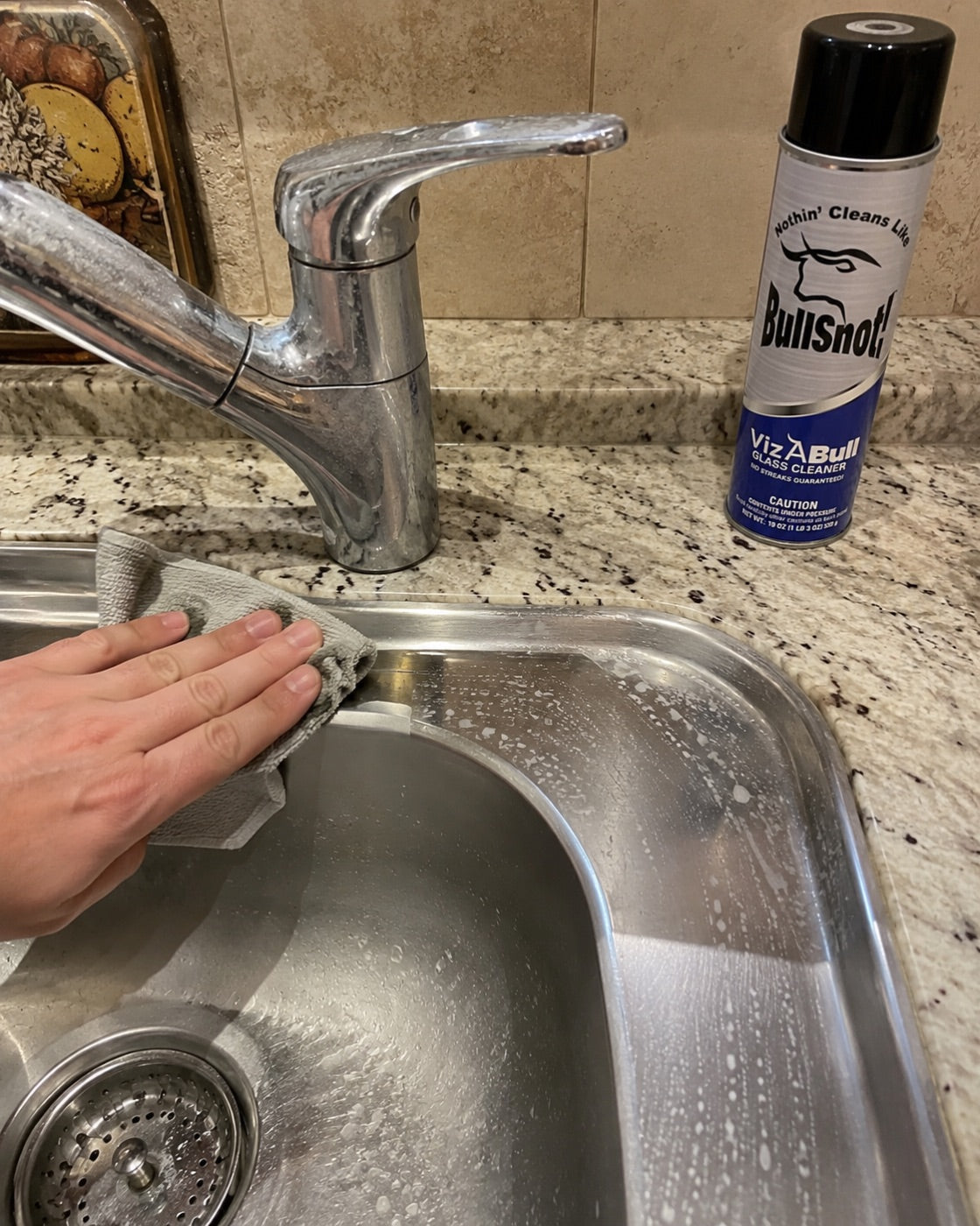 Stainless sink and chrome tap being cleaned with VizABull on the granite behind.