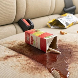 A spilled fruit punch box across a car seat with snacks